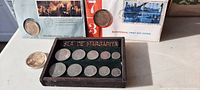Photo showing the Isla de Margarita coin set in a display box with eleven copper coins, two 1976 Bicentennial First Day Covers each with an affixed commemorative coin, and some loose individual coins on a white surface.