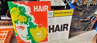 Front covers of the Hair musical book and Playbill booklet displayed side by side on a table with various items nearby.