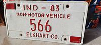 Front view of vintage 1983 Elkhart County non-motor vehicle licence plate showing embossing with red text and number 566 on white background with red reflectors at corners.