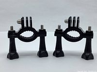 Front view of two black camera mounts showing clamps and mounting screws.