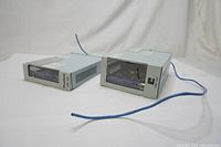 Two metal remote indoor enclosures laid on a white surface, showing front and side views with blue cables attached.