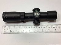 Side view of Excalibur Tact 100 crossbow scope with adjustment turrets visible and ruler showing approximately 21 cm length.