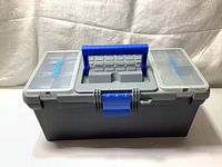 Closed gray and blue plastic toolbox with two lidded compartments on top and carry handle in center.