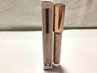 Tube of Nude By Nature Beach Glow Liquid Highlighter in shade 03 Sunrise with rose gold cap standing beside its box.