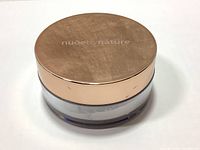 View of closed translucent loose finishing powder container with rose gold lid showing 'nude by nature' logo and scratches on lid.