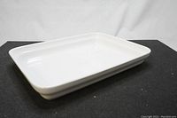 White rectangular stoneware baking dish with glossy finish shown from side angle on black background.