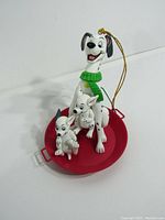 Front and side views of Disney 101 Dalmatians Christmas ornament showing adult Dalmatian with three puppies in a red sled and gold hanging string
