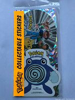 Photo of pack with Poliwhirl and trainers on holographic background, sealed in plastic packaging with yellow Pokemon Collectable Stickers label.