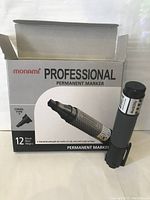 Open box showing one black Monami permanent marker with chisel tip beside the box.