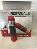 Box of 12 Monami Professional Permanent Markers in red with one marker positioned in front showing label and grip area.