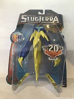 Front view of Slugterra Basic Flinger Joules figure in original packaging showing blue and yellow figure with blue stretchy launcher inside clear blister pack, branded with Slugterra logo and 'Shoots up to 20 ft' claim.