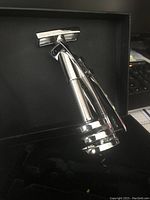 Silver wine bottle uncorking system positioned inside a black box, showing the handle and corkscrew in detail.