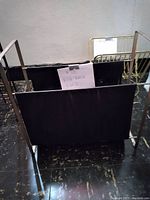 Front view of black metal book rack with solid panels and metal frame on floor against wall with paper label