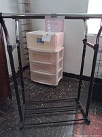 Four plastic stackable drawers, white with translucent fronts, shown stacked together in room corner next to shelf.
