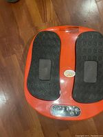 Top view of orange foot massager showing black textured foot pads and control buttons.