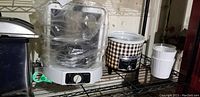 Photo of deep fryer, rotisserie oven wrapped in plastic, slow cooker, and white flour plant pot on shelving.