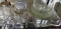 Shelf displaying clear glass bowls and plates, white ceramic teapot, glass jar with lid, decorative glass orb, and ceramic plates.