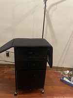 Close-up view of the ironing station with foldable board wings folded down, showing the three drawers and caster wheels.