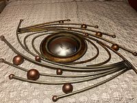 Full view of metal wall art sculpture showing curved rods with bronze spheres and central concave circular plate