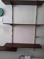 Three dark wood shelves mounted on the wall with metal brackets and vertical metal mounting tracks.