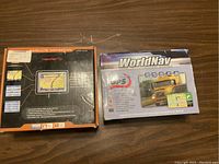 Two GPS trucker navigation units in their original boxes placed on a wooden surface.
