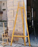 Tall wooden tripod easel beside two other easels showing relative sizes and structure.