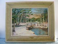 Frontal view of the original oil painting on board depicting a winter landscape with a wooden bridge over a stream, surrounded by leafless and evergreen trees, signed by Edna Snyder.