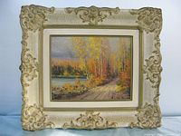 Framed oil painting showing vibrant autumn fall trees by lake with road path and forest background.