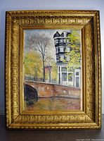 Full view of the framed oil painting showing the multi-storey building, bridge, and surrounding trees with autumn colors.