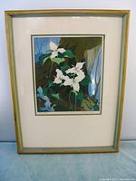 Photo showing the full framed print 'Trilliums' with wooden frame and glass cover on a table.