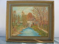 View of original oil painting on board framed, showing an autumn mill scene with a blue river, water wheel on a beige mill building, autumn colored trees, and pathway on the right side. Frame is gold-toned with light paint nicks visible.