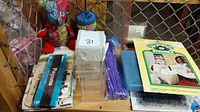 Overview of assorted craft supplies including patchwork bear, yarn skein, stencils, purple sticks, plastic containers, and packaged items