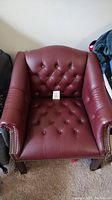 Full view of maroon leather tufted den chair with nailhead trim and wooden legs.