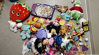 Overhead view of mixed toy lot including stuffed animals, dolls, and various figurines spread out on floor.