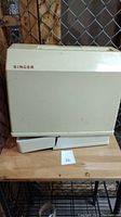 Beige carrying case for the Singer sewing machine with the Singer logo visible.