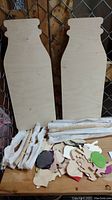 Large wooden milk jug shaped boards, small wooden painted and unpainted cutouts, several wooden snakes wrapped in tissue paper on wooden surface