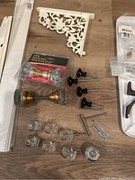 Top view of various door knobs, black pull handles, decorative white corner bracket, and clear plastic clip rings.