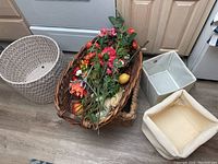 Three large baskets in natural woven materials and two square IKEA fabric storage bins with artificial flowers in one basket shown together on floor.