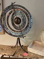 Full view of bronze sphere sculpture on textured stone surface with tripod base and visible glass inlays.