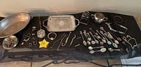 Overview photo showing a collection of silver plated flatware, serving pieces, small trays, bowls, cups, and multiple pieces of vintage jewelry including earrings, bracelets, a watch, and coat pins.