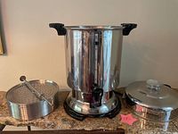 Front view of Hamilton Beach commercial coffee urn with filter basket and stirring spoon placed beside it on countertop.
