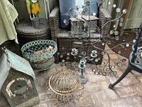 Overview of lot shows multiple iron outdoor decor items including birdhouse, hanging planter, candleabra, and candle lamps, with cushions in background.