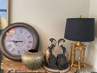 Full view showing round wall clock, bronze style lamp with black shade, lacquer jar, and two hand painted corbels or bookends on table