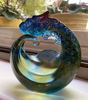 Side view of the blue-green crystal dragon sculpture on a window sill with plants in background.