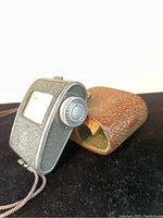 Close-up of Exposimet light meter with leather case showing metal body and textured leather worn case.