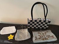 Four vintage hand beaded clutches including black and silver checkered bag, silver and brown tree design clutch, silver metallic clutch, and white floral beaded clutch