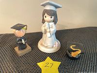 Group photo showing all four items: the Precious Moments graduate bobblehead, small glass graduate bobblehead, porcelain trinket cap, and graduation cap ring case.