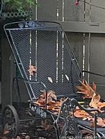 Front view of the vintage wrought iron recliner chair showing the mesh back and seat with rose pattern decoration and some leaves on the seat.