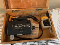 Top view of vintage US Navy Fairchild M4 gun sight camera assembly inside original wooden box with paperwork and small boxes of accessories.