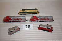 Top down photo of all five engines arranged on striped surface showing a group view of the lot, with two large Santa Fe engines, one small Santa Fe engine, one red and silver engine, and one yellow and green Westinghouse engine visible.